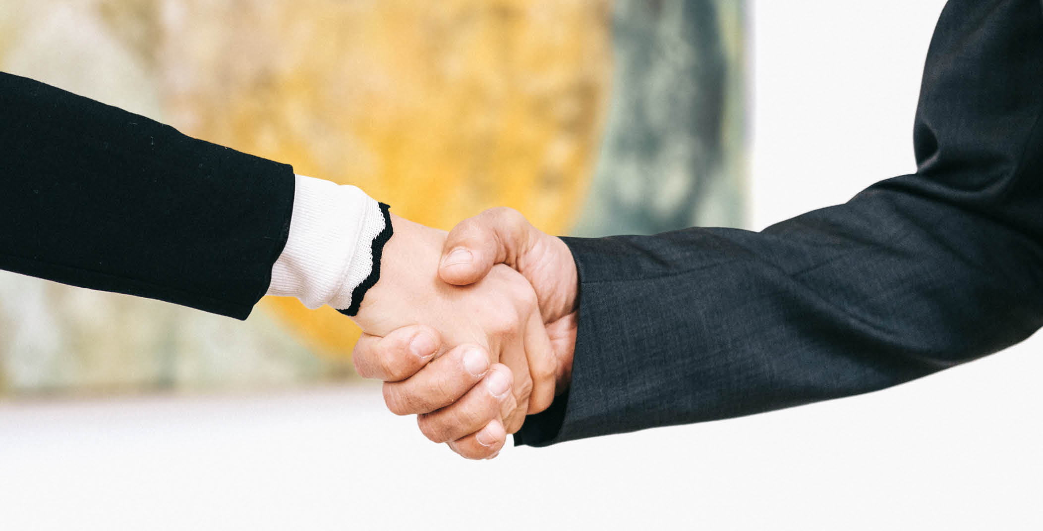 Handschlag einer Frauen- und Männerhand mit unscharf sichtbarem Kunstwerk im Hintergrund