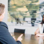 Mag. Gerwald Holper und Mag. Nicole Panis-Markom sitzen am Verhandlungstisch und kommunizieren. Kunstwerk im Hintergrund